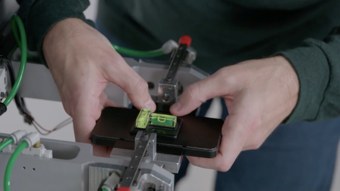 Corning worker holding a demonstration phone with Gorilla Glass on a testing rig, with spirit levels resting on top.